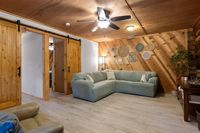 living room with a barn door, wood walls, ceiling fan, and light hardwood / wood-style floors