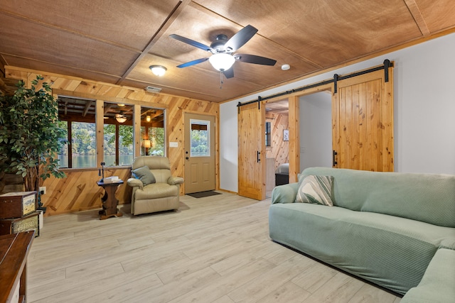 living room featuring a barn door, light hardwood / wood-style flooring, ceiling fan, and wood walls