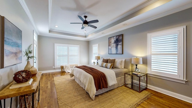 bedroom featuring ceiling fan, crown molding, light hardwood / wood-style flooring, and a tray ceiling