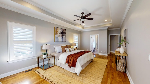 bedroom featuring ensuite bathroom, ceiling fan, a raised ceiling, ornamental molding, and light hardwood / wood-style flooring