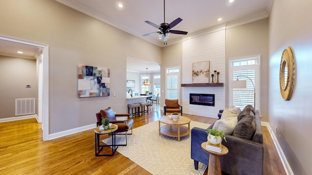 living room with a wealth of natural light, light hardwood / wood-style floors, ornamental molding, and a towering ceiling