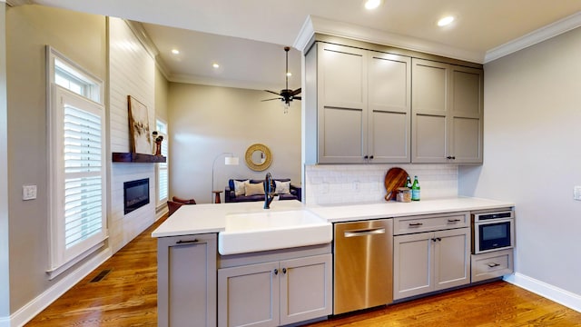 kitchen featuring gray cabinets, stainless steel appliances, decorative backsplash, a large fireplace, and sink