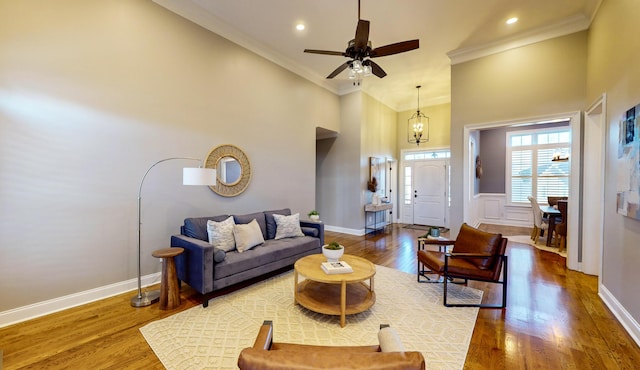 living room with ceiling fan with notable chandelier, a high ceiling, hardwood / wood-style floors, and crown molding