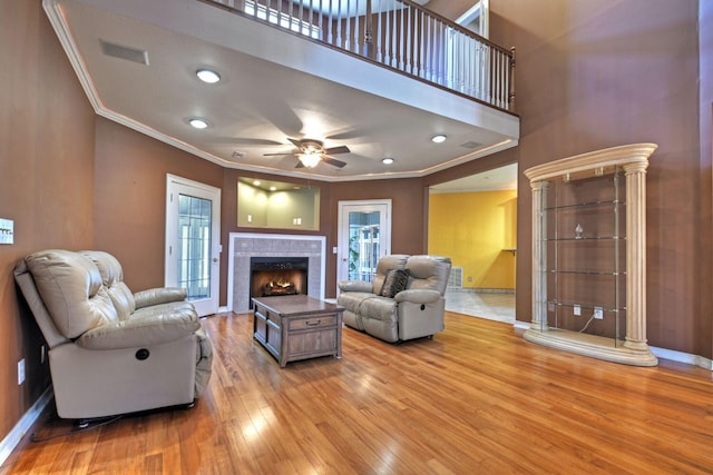 living room featuring light hardwood / wood-style flooring, ceiling fan, ornamental molding, and a tiled fireplace