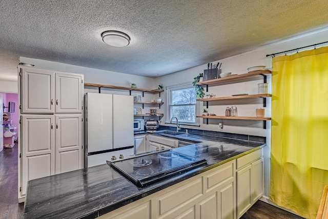 kitchen featuring dark countertops, freestanding refrigerator, black electric cooktop, open shelves, and a sink