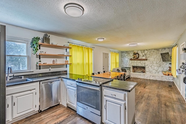 kitchen featuring a peninsula, dark countertops, appliances with stainless steel finishes, and open shelves