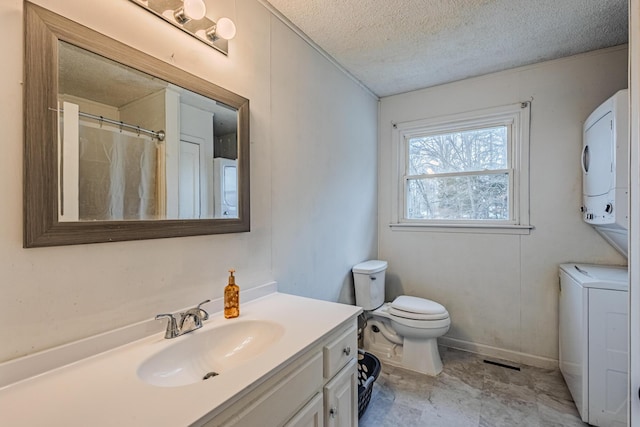 bathroom with a textured ceiling, toilet, vanity, baseboards, and stacked washer and clothes dryer