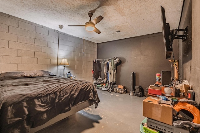 bedroom featuring concrete block wall, concrete floors, and a ceiling fan