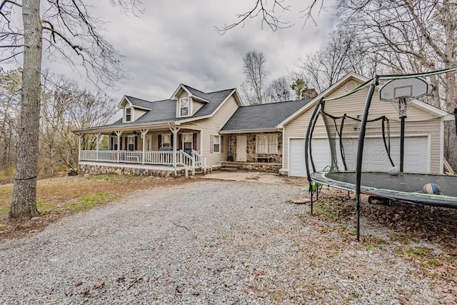 view of front of property featuring a trampoline, gravel driveway, a chimney, a porch, and a garage