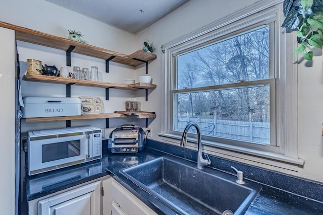 kitchen featuring dark countertops, white cabinetry, open shelves, and a sink