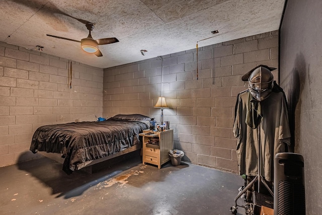 bedroom featuring a ceiling fan, concrete block wall, and unfinished concrete floors