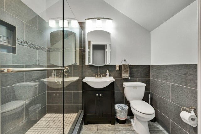 bathroom featuring a shower with door, vanity, tile walls, and toilet