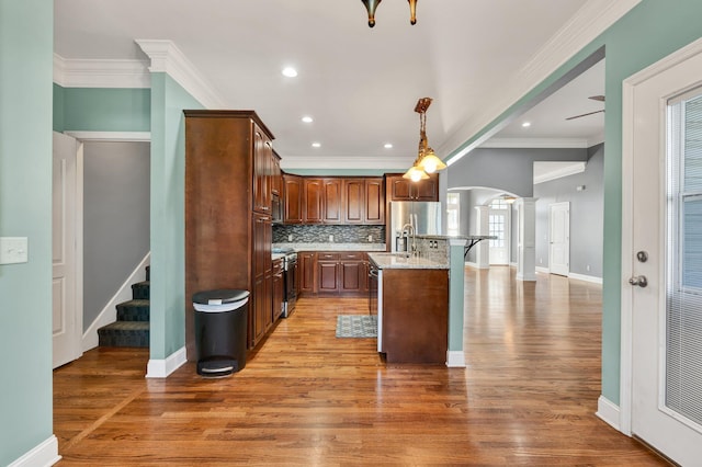 kitchen featuring appliances with stainless steel finishes, ornamental molding, decorative light fixtures, a center island with sink, and dark hardwood / wood-style floors