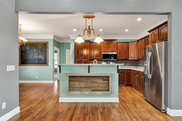 kitchen with an island with sink, a chandelier, light hardwood / wood-style floors, decorative light fixtures, and appliances with stainless steel finishes