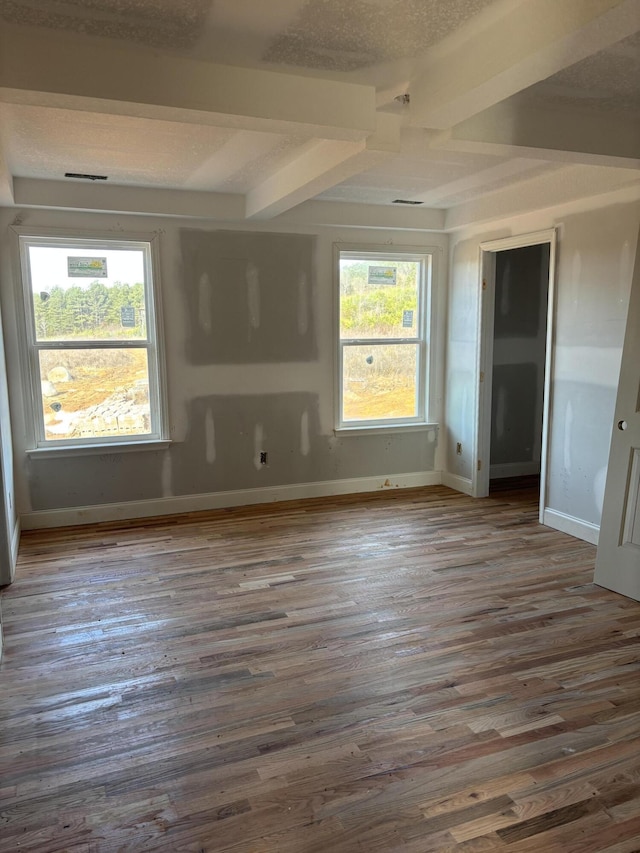 unfurnished bedroom featuring multiple windows, baseboards, wood finished floors, and beamed ceiling