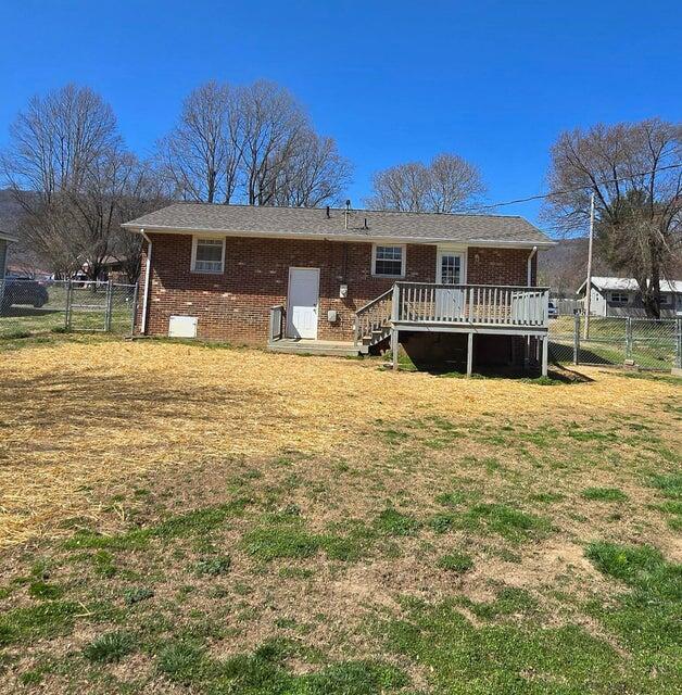 back of house with brick siding, a wooden deck, fence, and a gate