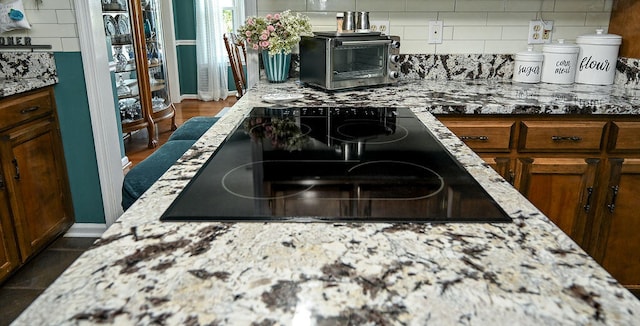 kitchen with black electric stovetop, decorative backsplash, and light stone counters