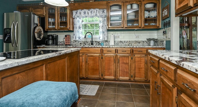 kitchen featuring stainless steel fridge, light stone countertops, black electric cooktop, and backsplash