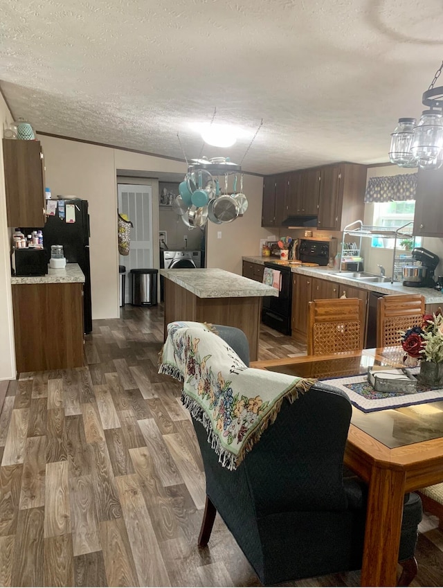 kitchen with a center island, black appliances, independent washer and dryer, a textured ceiling, and dark hardwood / wood-style flooring