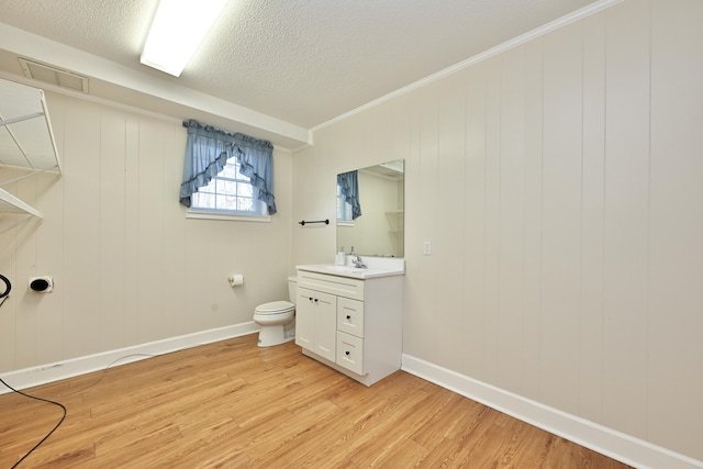 bathroom with wood-type flooring, ornamental molding, vanity, toilet, and a textured ceiling