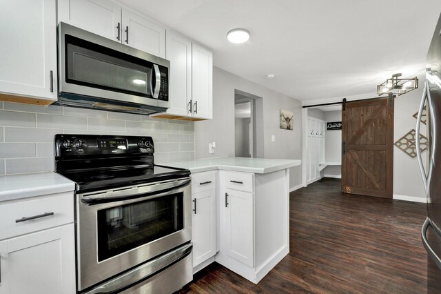 kitchen with light countertops, tasteful backsplash, stainless steel appliances, dark wood-type flooring, and a barn door