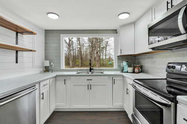 kitchen featuring light countertops, open shelves, stainless steel appliances, decorative backsplash, and a sink