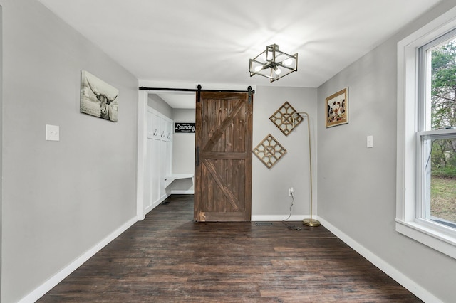 unfurnished dining area featuring dark wood-style flooring, a notable chandelier, baseboards, and a barn door