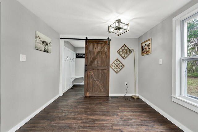unfurnished dining area featuring baseboards, a barn door, dark wood-type flooring, and a chandelier