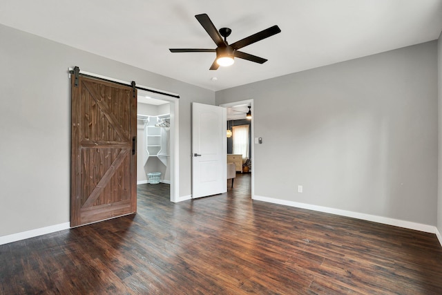 unfurnished bedroom featuring a closet, baseboards, wood finished floors, a barn door, and a spacious closet