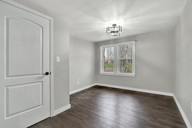 unfurnished dining area with dark wood-style flooring, a notable chandelier, baseboards, and visible vents