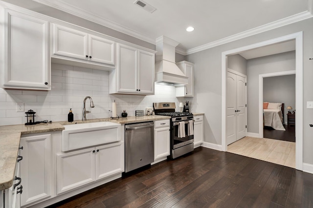 kitchen with stainless steel appliances, white cabinetry, premium range hood, and light stone counters