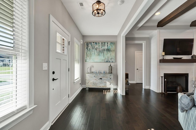 foyer entrance featuring beamed ceiling, dark hardwood / wood-style flooring, a large fireplace, and an inviting chandelier