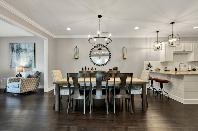 dining area featuring sink, dark wood-type flooring, a notable chandelier, and ornamental molding