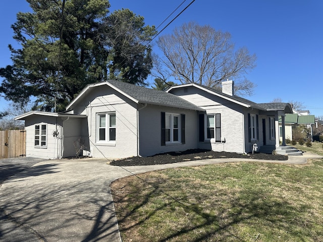 view of side of property featuring a lawn, driveway, fence, brick siding, and a chimney