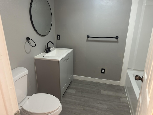 full bathroom featuring toilet, a bathing tub, wood finished floors, baseboards, and vanity