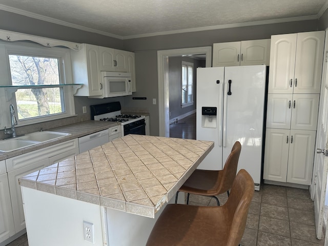 kitchen featuring a center island, tile counters, white appliances, white cabinetry, and a sink