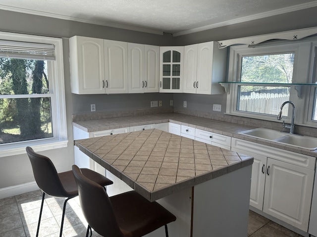 kitchen with a wealth of natural light, a textured ceiling, white cabinetry, and a sink