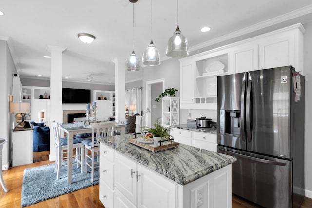 kitchen with a center island, stainless steel refrigerator with ice dispenser, wood finished floors, ceiling fan, and light stone countertops