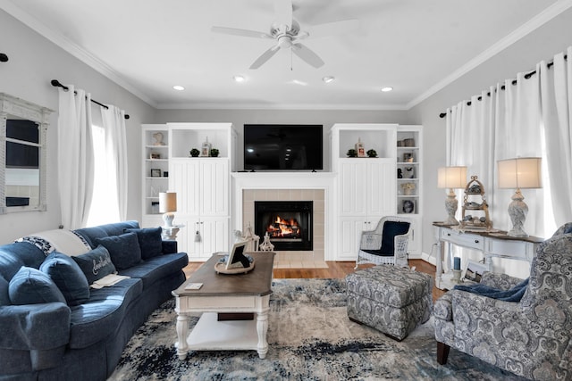 living room with ceiling fan, recessed lighting, wood finished floors, ornamental molding, and a tiled fireplace