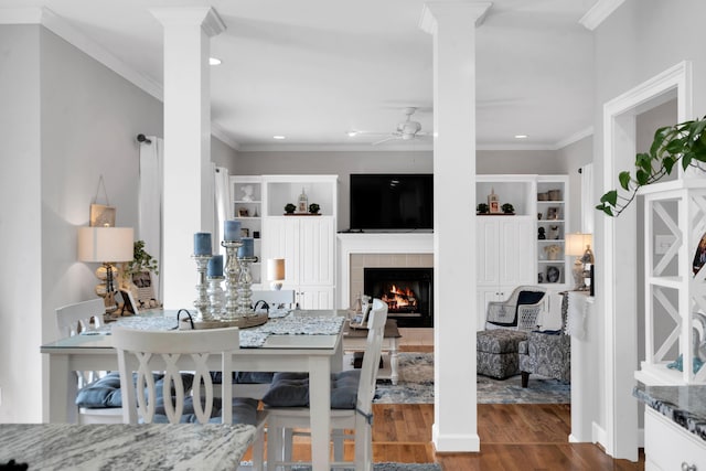 interior space with ceiling fan, a fireplace, wood finished floors, decorative columns, and crown molding