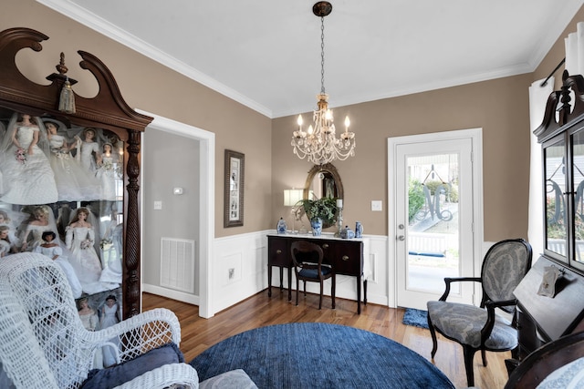 sitting room featuring visible vents, a wainscoted wall, ornamental molding, wood finished floors, and an inviting chandelier