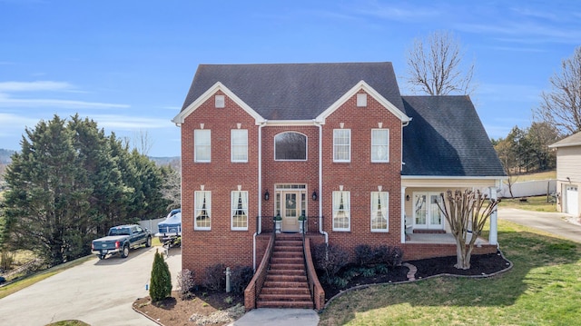 view of front of property with concrete driveway, french doors, a shingled roof, and brick siding