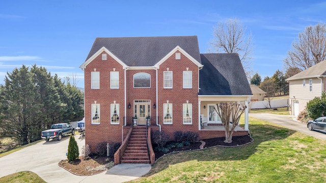 view of front of property with driveway, brick siding, a front yard, and a shingled roof