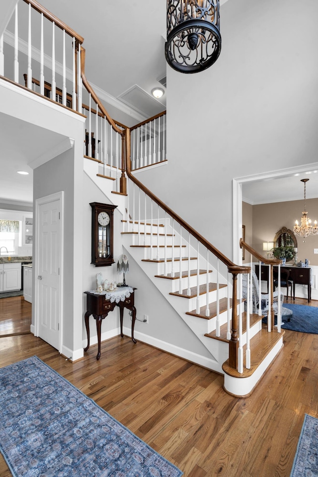 stairs featuring crown molding, a notable chandelier, baseboards, and wood finished floors