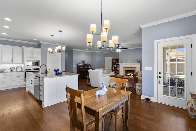 dining area with ceiling fan with notable chandelier, dark wood-type flooring, crown molding, and sink