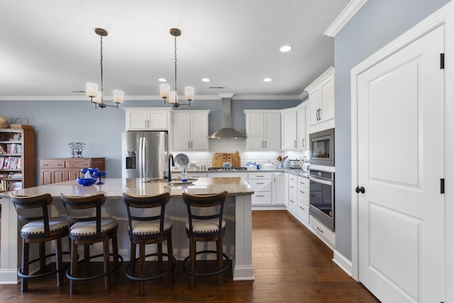 kitchen featuring a kitchen island with sink, wall chimney range hood, decorative backsplash, white cabinetry, and stainless steel appliances