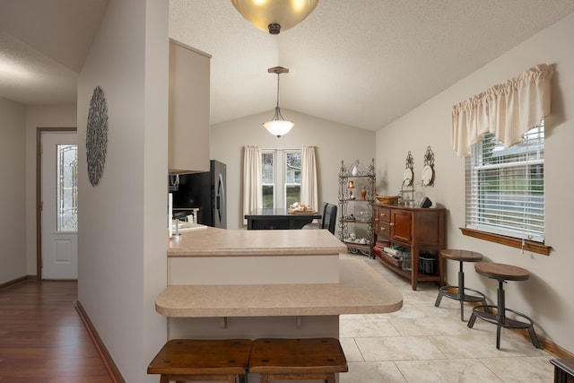 kitchen featuring black fridge, a peninsula, a textured ceiling, and lofted ceiling