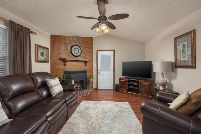 living area featuring a ceiling fan, lofted ceiling, a fireplace, dark wood-type flooring, and a textured ceiling