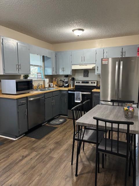 kitchen featuring gray cabinetry, a textured ceiling, appliances with stainless steel finishes, and dark wood-type flooring