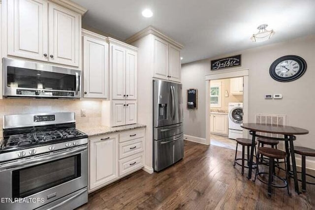 kitchen with washer / clothes dryer, appliances with stainless steel finishes, light stone countertops, dark hardwood / wood-style floors, and tasteful backsplash